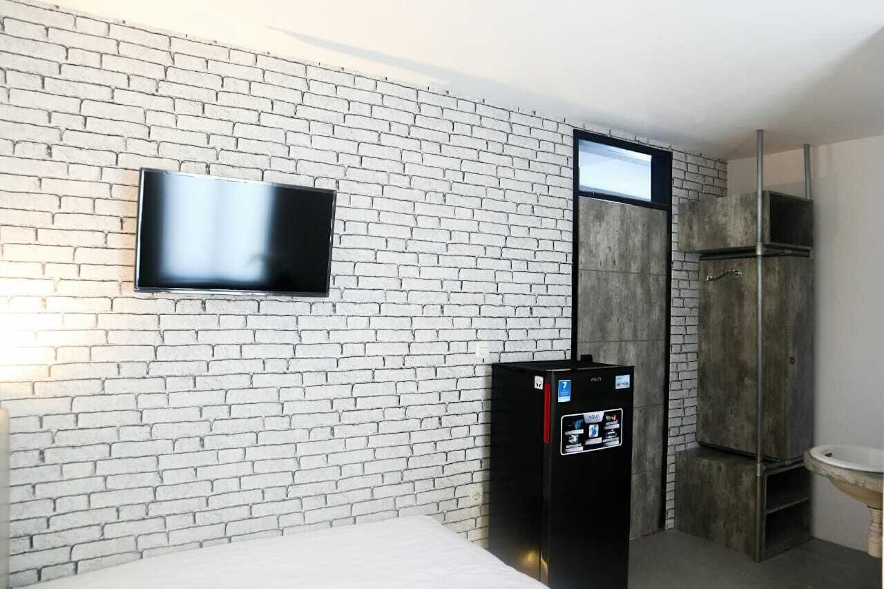 Ein modernes Badezimmer mit einer weißen Ziegelwand, einem flachbildfernseher über einem schwarzen Kühlschrank und einem großen Spiegel.