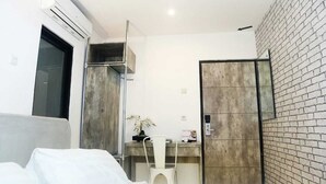Una habitación de hotel moderna con una cama, un escritorio, una silla, un equipo de aire acondicionado, un armario y una pared de ladrillo.