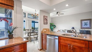 Una cocina con lavavajillas, encimeras de granito, armarios de madera y un comedor con mesa y sillas.