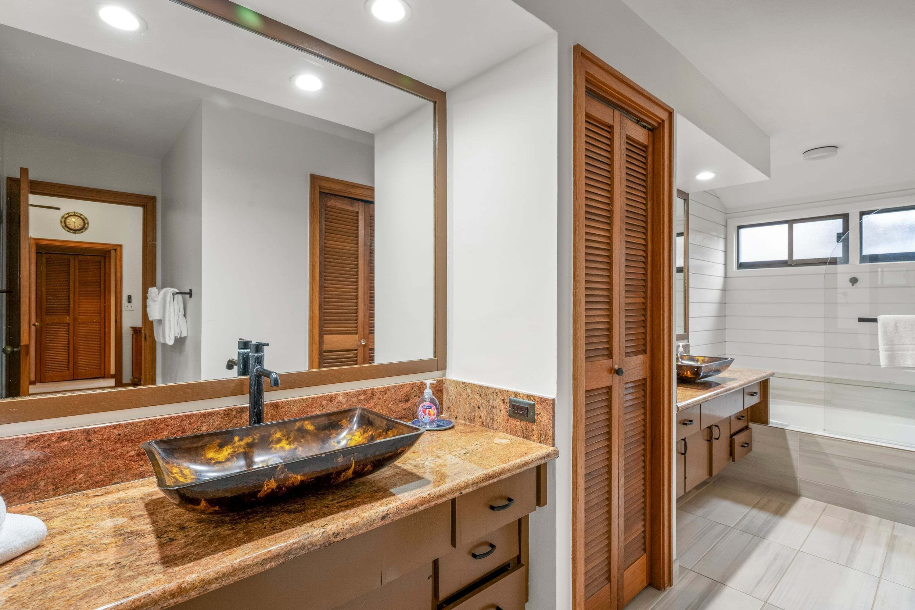 A modern bathroom with a large mirror, a vessel sink, wooden cabinets, and a bathtub.