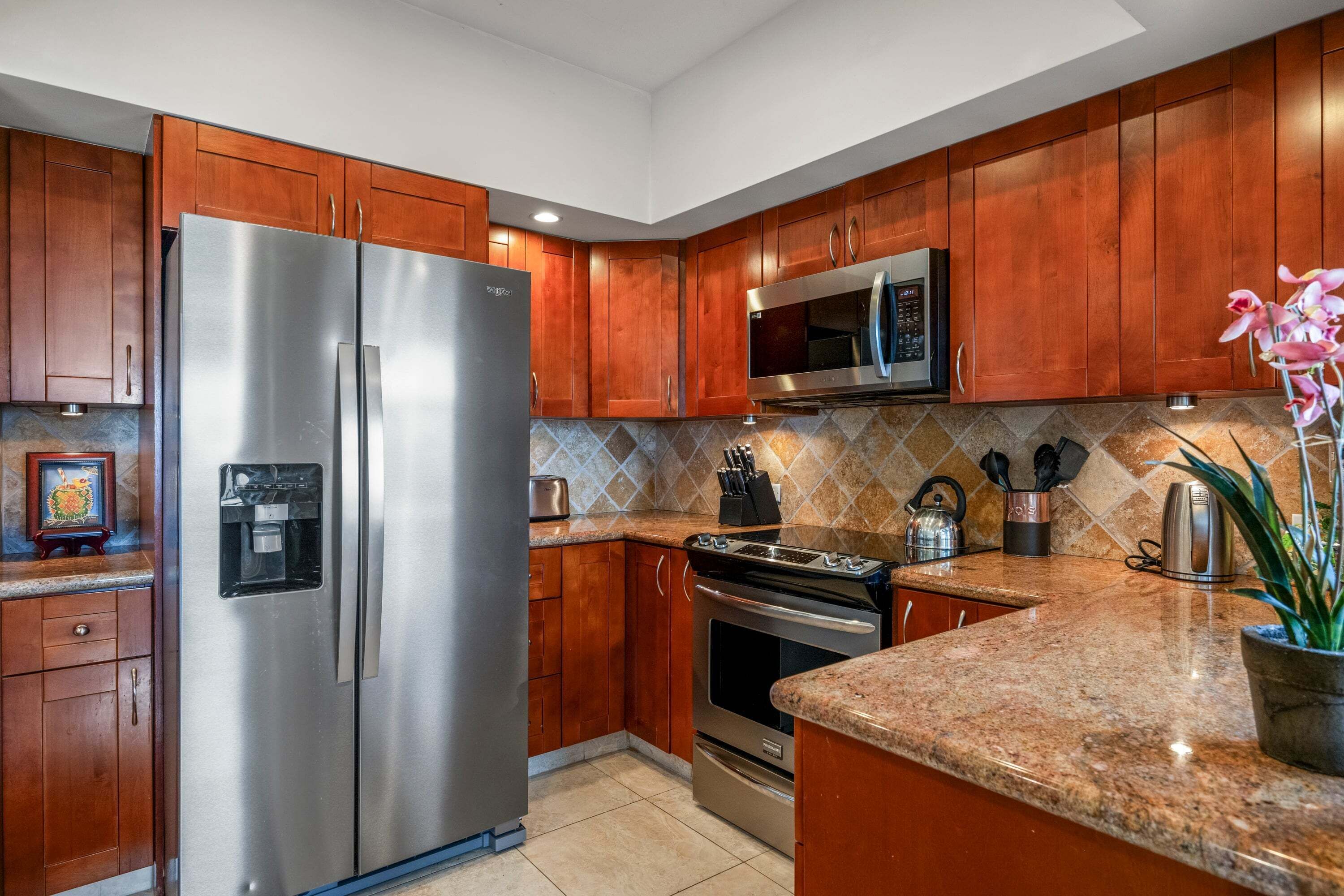Una cocina con armarios de madera, electrodomésticos de acero inoxidable, encimera de granito y una planta en maceta.