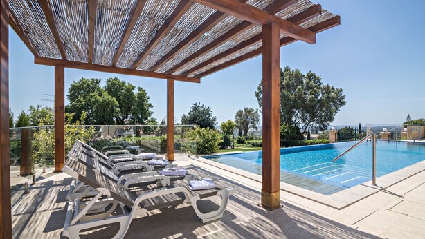 Un área junto a la piscina con sillones de descanso y una pérgola.