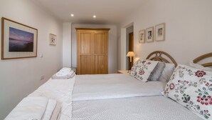 Un dormitorio con cama, almohadas, una mesita de noche, lámpara, armario de madera y cuadros en la pared.