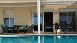 Zona de piscina con mobiliario exterior, un porche cubierto y la entrada de un edificio.