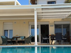 A poolside area with outdoor furniture, a covered patio, and a building entrance.