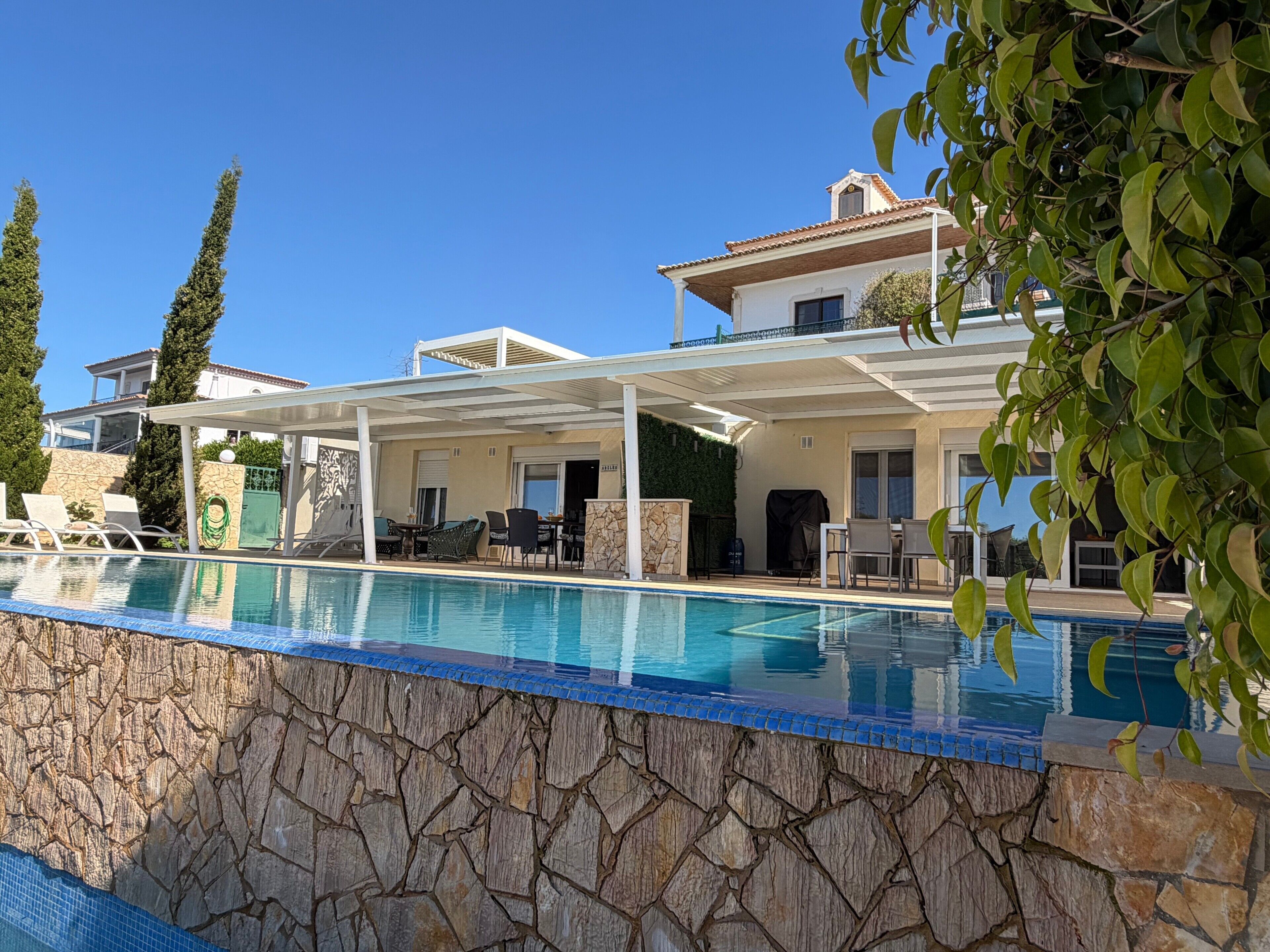 A poolside area with a stone wall, lounge chairs, and a covered patio.