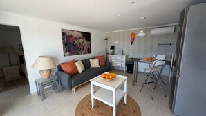 Un salon moderne comprenant un canapé, une table basse, un coin repas avec des chaises, un réfrigérateur et un tableau accroché au mur.