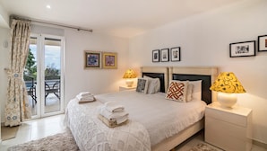 Une chambre à coucher comprenant un lit, deux lampes de chevet, une table de chevet, une fenêtre avec des rideaux et une vue sur un patio extérieur.