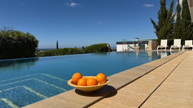Une piscine avec un saladier rempli d’oranges posé sur le bord, des chaises longues et une vue sur l’océan.