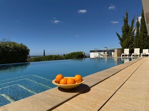 Una piscina con un cuenco de naranjas en el borde, sillas de descanso y vistas al océano.