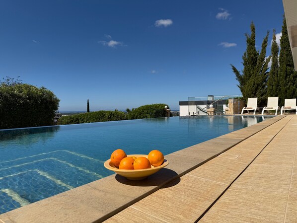 A swimming pool with a bowl of oranges on the edge, lounge chairs, and a view of the ocean.