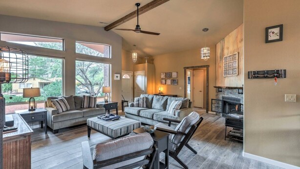 A spacious living room with a fireplace, large windows, and a ceiling fan.