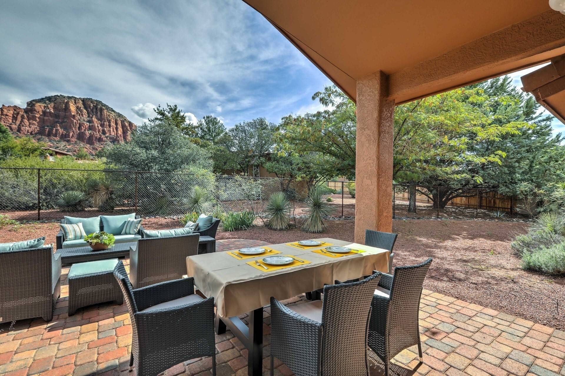 An outdoor patio with wicker furniture, a table set for dining, and a view of a mountainous landscape.