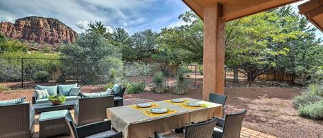 An outdoor patio with wicker furniture, a table set for dining, and a view of a mountainous landscape.