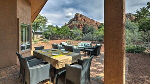 An outdoor patio with a table set for dining, surrounded by wicker furniture, and a view of red rock formations in the background.