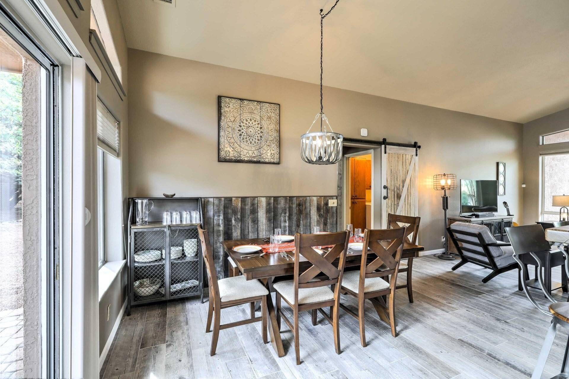 A dining area with a wooden table and chairs, a chandelier, and a rustic wall panel.