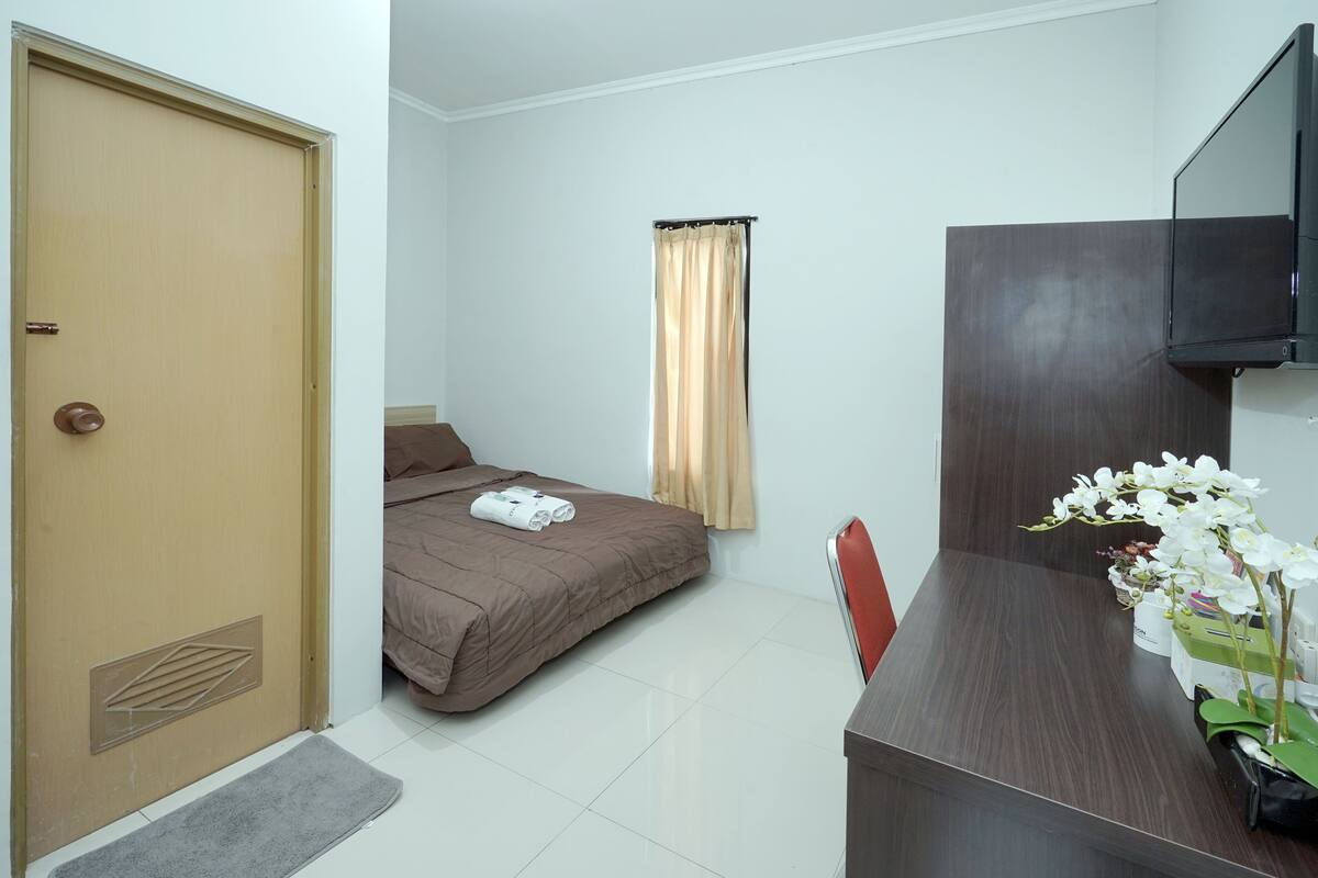 Habitación de hotel con cama, escritorio con computadora, televisor y ventana con cortinas.