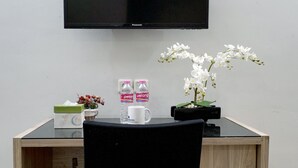 A wooden desk with a black chair, a television mounted on the wall, a small potted orchid, and two bottles of water. - Dparagon Mt Haryono (Semarang)