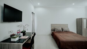 A modern hotel room with a flat-screen TV mounted on the wall, a wooden desk with a chair, a bed with a brown bedspread, and a wardrobe. - Dparagon Mt Haryono (Semarang)