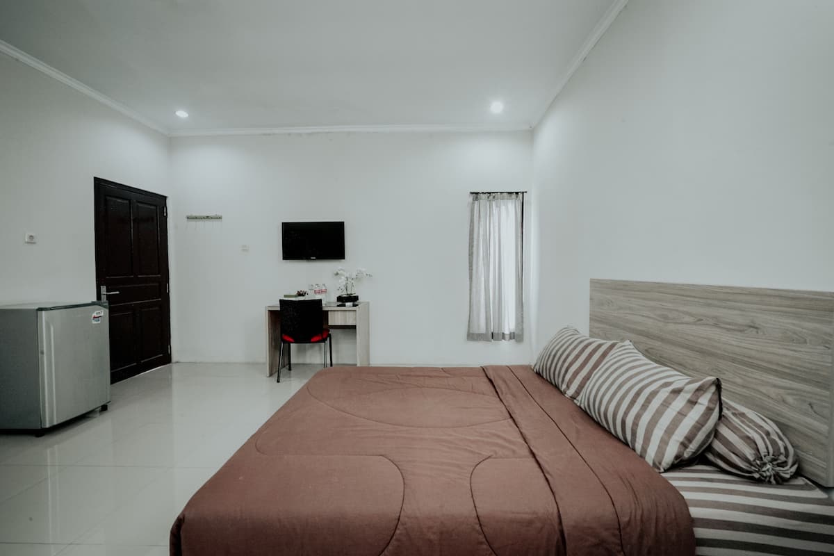 Un dormitorio con cama, escritorio, televisión y refrigerador.