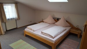 Une chambre avec un lit simple, un cadre en bois, une table de chevet avec une lampe, une fenêtre avec des rideaux et un radiateur.