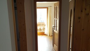 Un couloir avec un tapis à rayures, des portes en bois et une vue sur une autre pièce où se trouvent un lit et des rideaux.