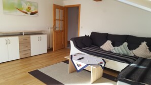 Un salon comprenant un canapé, une table basse et un coin cuisine avec des placards et un radiateur.