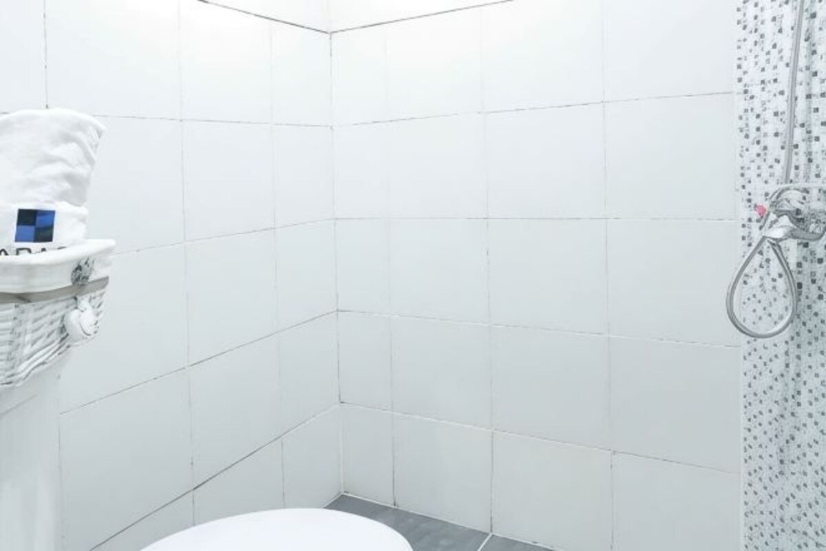 A small, white-tiled bathroom with a toilet, a shower with a handheld showerhead, and a towel rack with a towel.