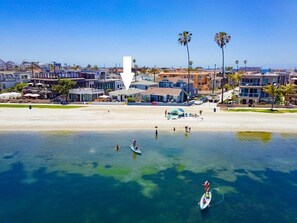 A coastal area with a beach, paddleboarders, and residential buildings.