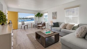 A modern living room with a grey sofa, a wooden coffee table, and a view of the sea through large windows.