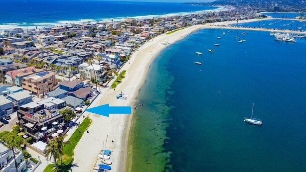 An aerial view of a coastal town with a beach, marina, and residential buildings.