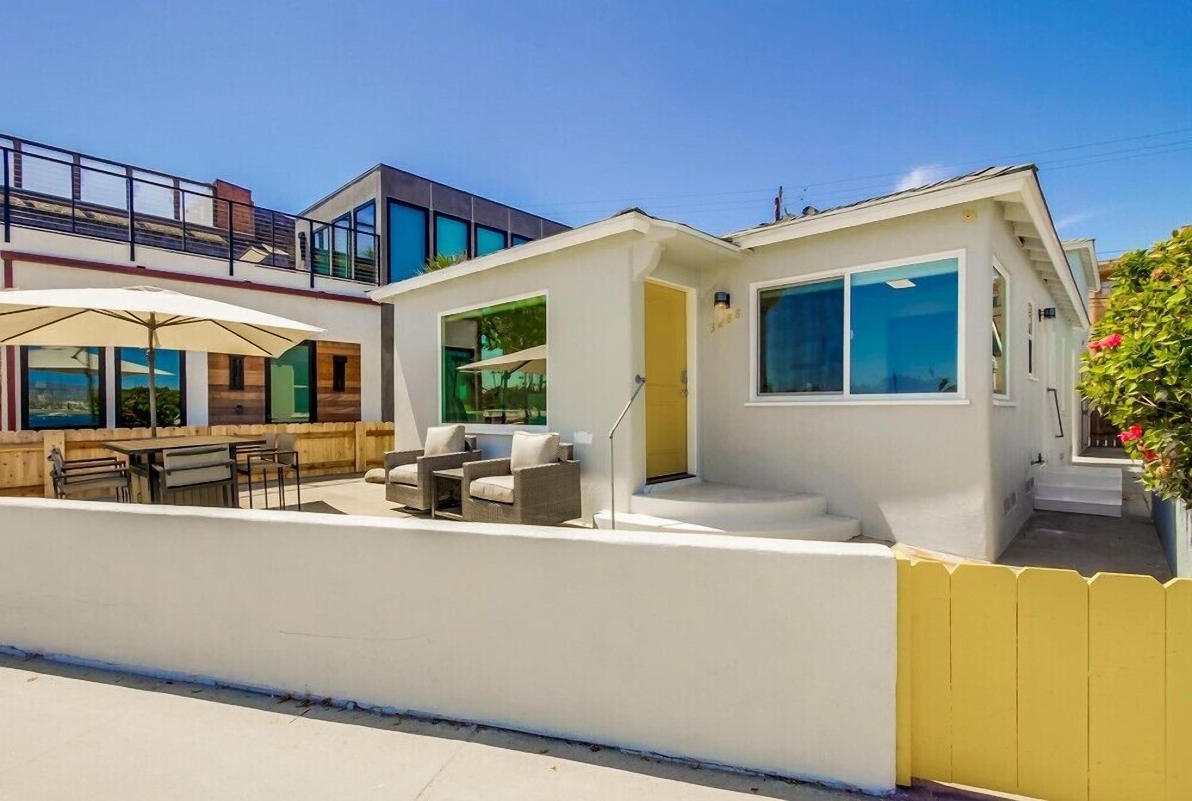 A modern two-story house with a patio area featuring outdoor furniture and a large umbrella.