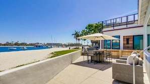 A patio with outdoor furniture overlooking a beach with boats.