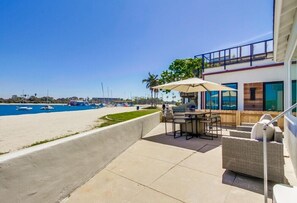 Pátio com mobiliário externo com vista para uma praia e barcos.