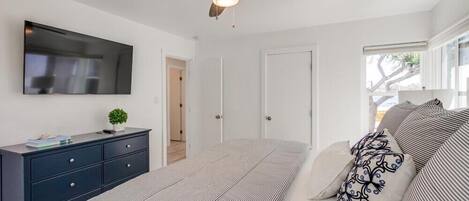 Un dormitorio con cama, tocador, ventilador de techo, televisor y ventana.