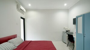 Een slaapkamer met een rode bed, een bureau met stoel, een kledingkast en een airconditioning.