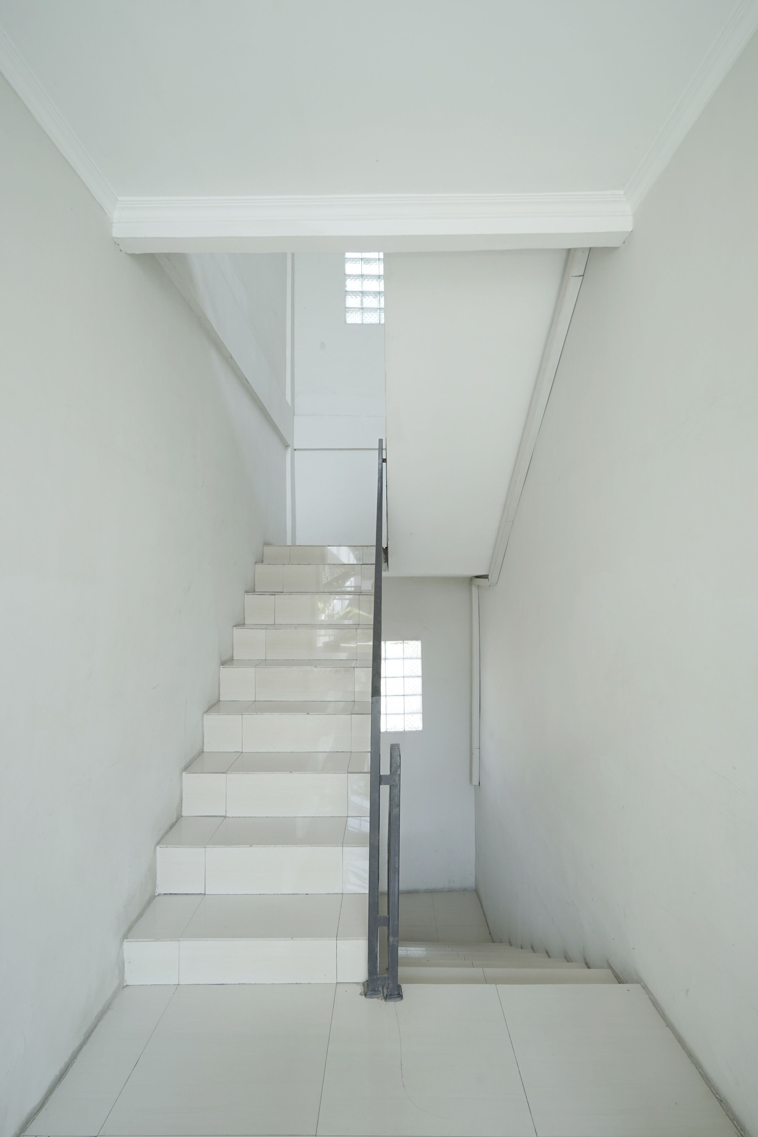 Un escalier avec des murs blancs et une rampe en métal.
