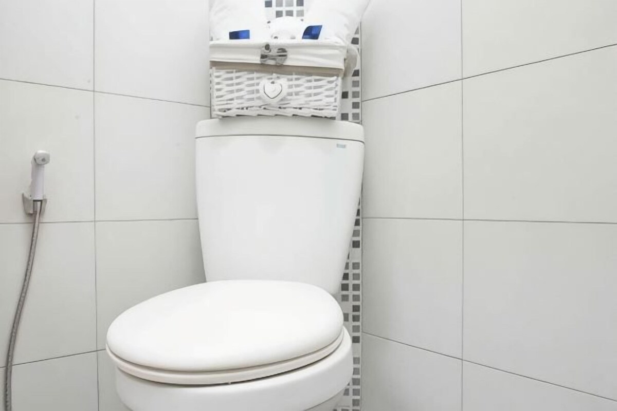 A white toilet with a lid, a shower hose, and a white tiled wall.