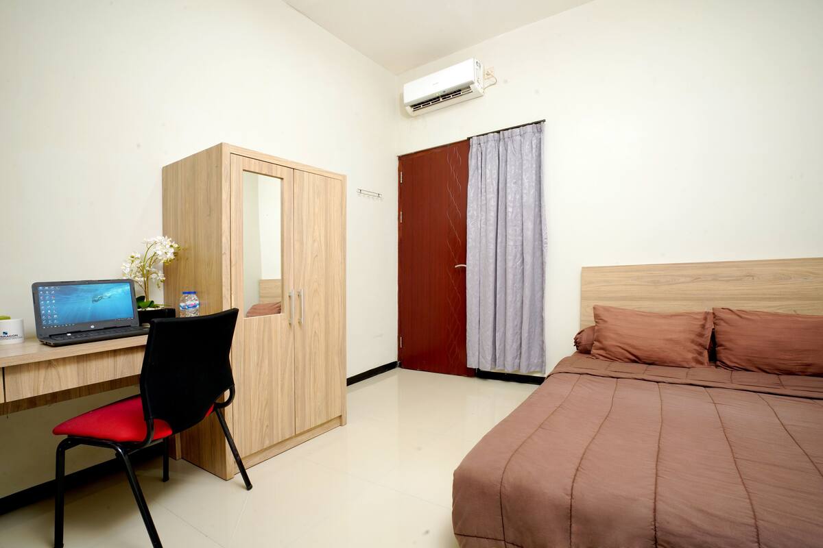 Un dormitorio con una cama, un escritorio con una computadora portátil, una silla, un armario y una cortina.