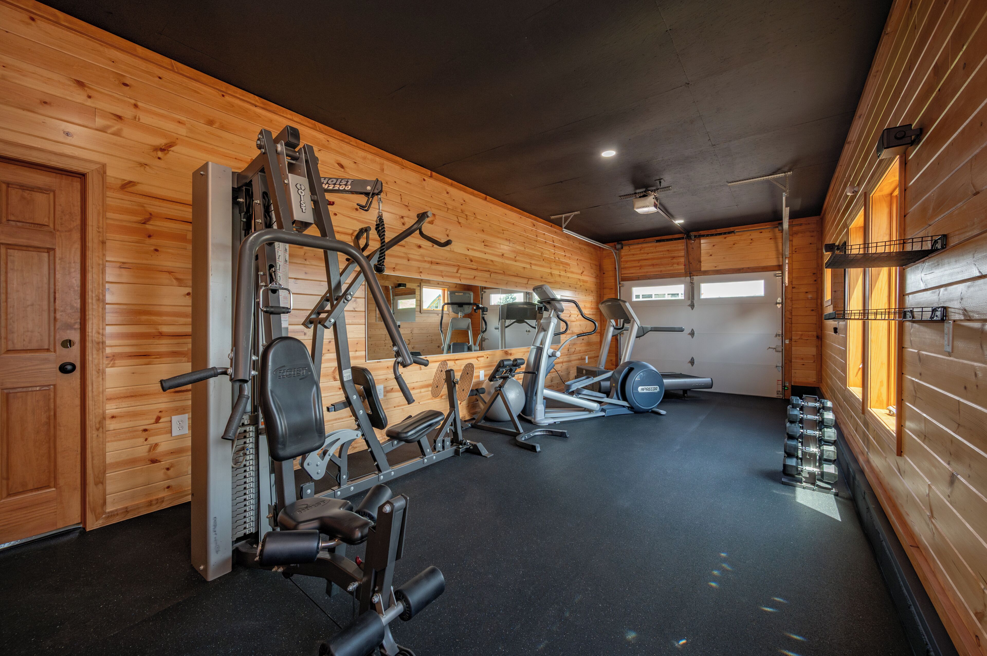 A gym with various exercise machines, a mirror, and a window with natural light.
