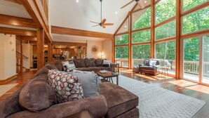 A spacious living room with a large sectional sofa, a ceiling fan, and large windows offering a view of the outdoors. - Lake Days & Game Nights w/ Hot Tub (Oakland)