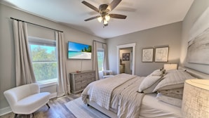 Ein Schlafzimmer mit Bett, Sessel, Schminktisch, Fernseher und Deckenventilator.