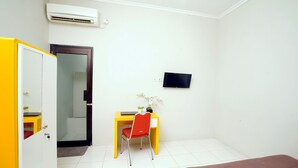 Una habitación con cama, un escritorio con silla, un televisor y un aire acondicionado.