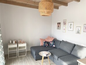 A modern living room with a grey sofa, a round side table, a white side table with glass candle holders, and a woven light fixture.