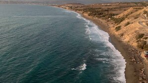 A coastal landscape with a beach, ocean, and distant mountains.