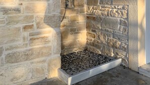 A stone-walled shower area with a metal grate floor and a white door frame.