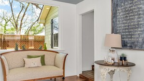 A cozy room with a cushioned chair, a small table with a lamp, and a large chalkboard with writing. - White Rabbit | Amazing Outdoor Area w/ Large Fire Pit | Hot Tub (Fredericksburg)