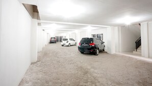 A parking garage with multiple cars parked in rows, white walls, and a tiled floor.