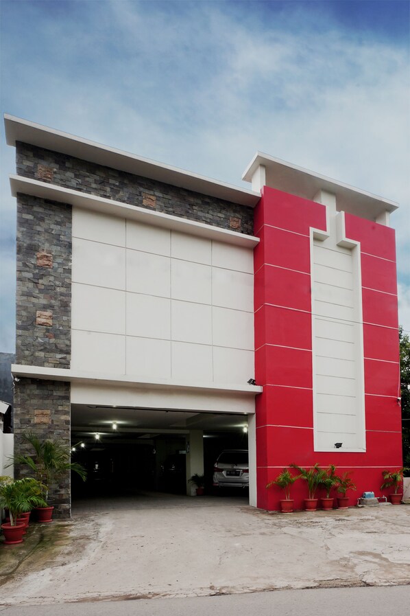 Un edificio moderno con fachada roja y blanca, un garaje y varias plantas en macetas.