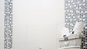 A white toilet with a basket of toiletries on the tank, black tiled floor, and a tiled wall with a mosaic pattern.
